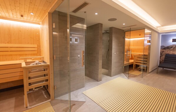 A modern sauna with glass walls, wooden benches, and a separate relaxation area with a sofa.