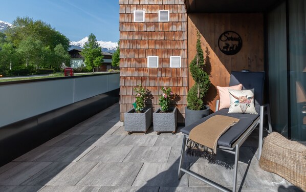 Una terraza en la azotea con un muro de madera, plantas en macetas, un banco y un sofá.