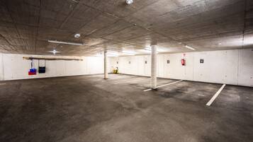 Een ondergrondse parkeergarage met betonnen vloeren en muren, aangeduid parkeerplaatsen en veiligheidsmiddelen zoals brandblussers.