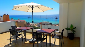 A balcony with two tables and chairs, a large umbrella, and a potted plant.