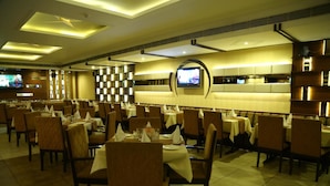 A restaurant with multiple tables and chairs, a television mounted on the wall, and a modern ceiling design. - Hotel Park Inn (Chandigarh)