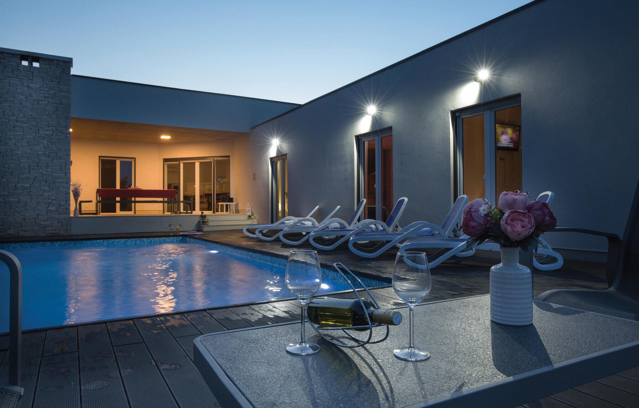 A poolside area with lounge chairs, a table with wine glasses and a bottle, and a flower vase.