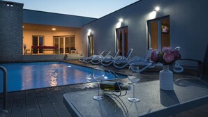 A poolside area with lounge chairs, a table with wine glasses and a bottle, and a flower vase. - Lovely home in Marici with sauna (Marici)