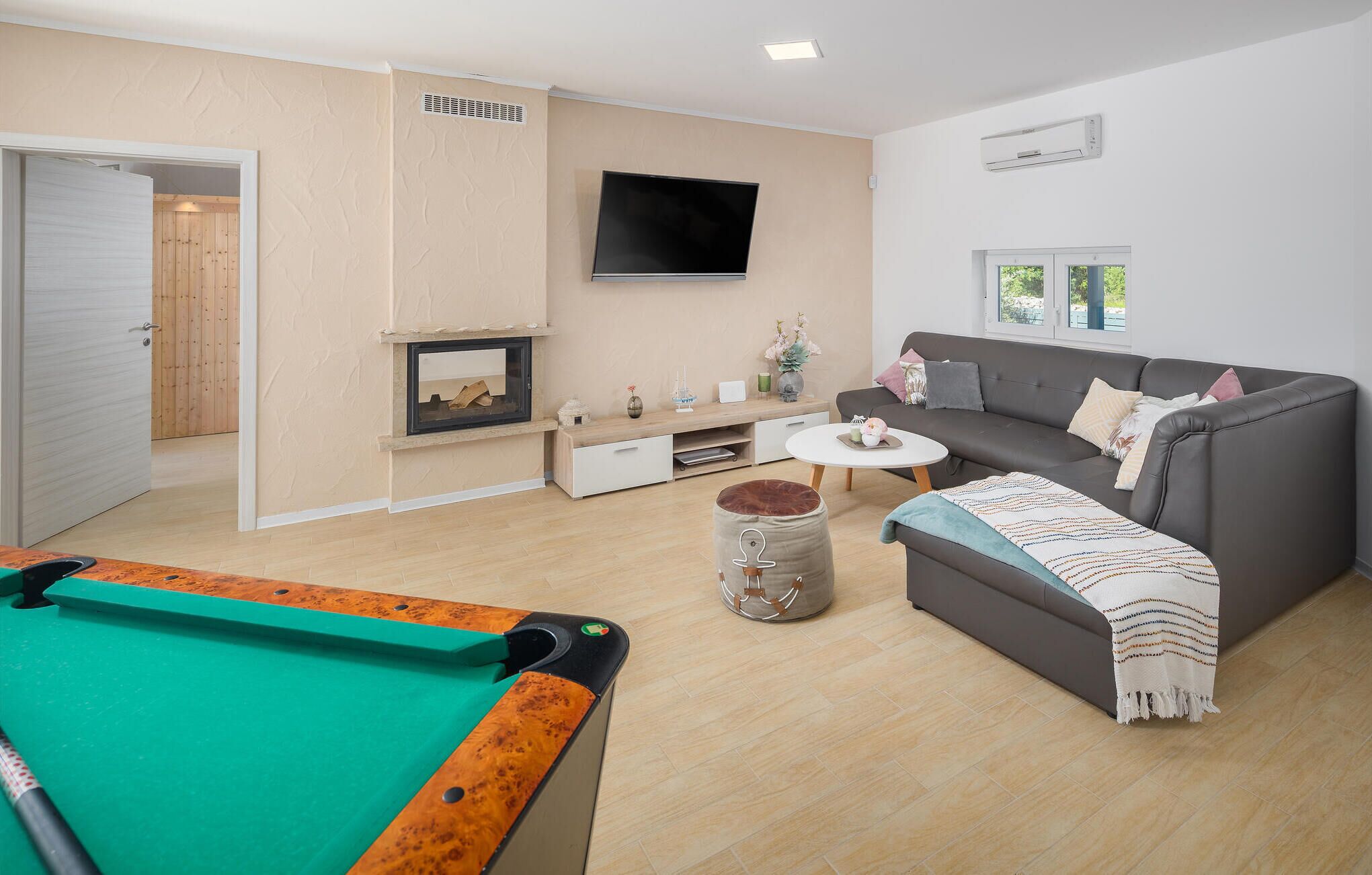 A living room with a pool table, a sofa, a coffee table, a fireplace, and a TV.