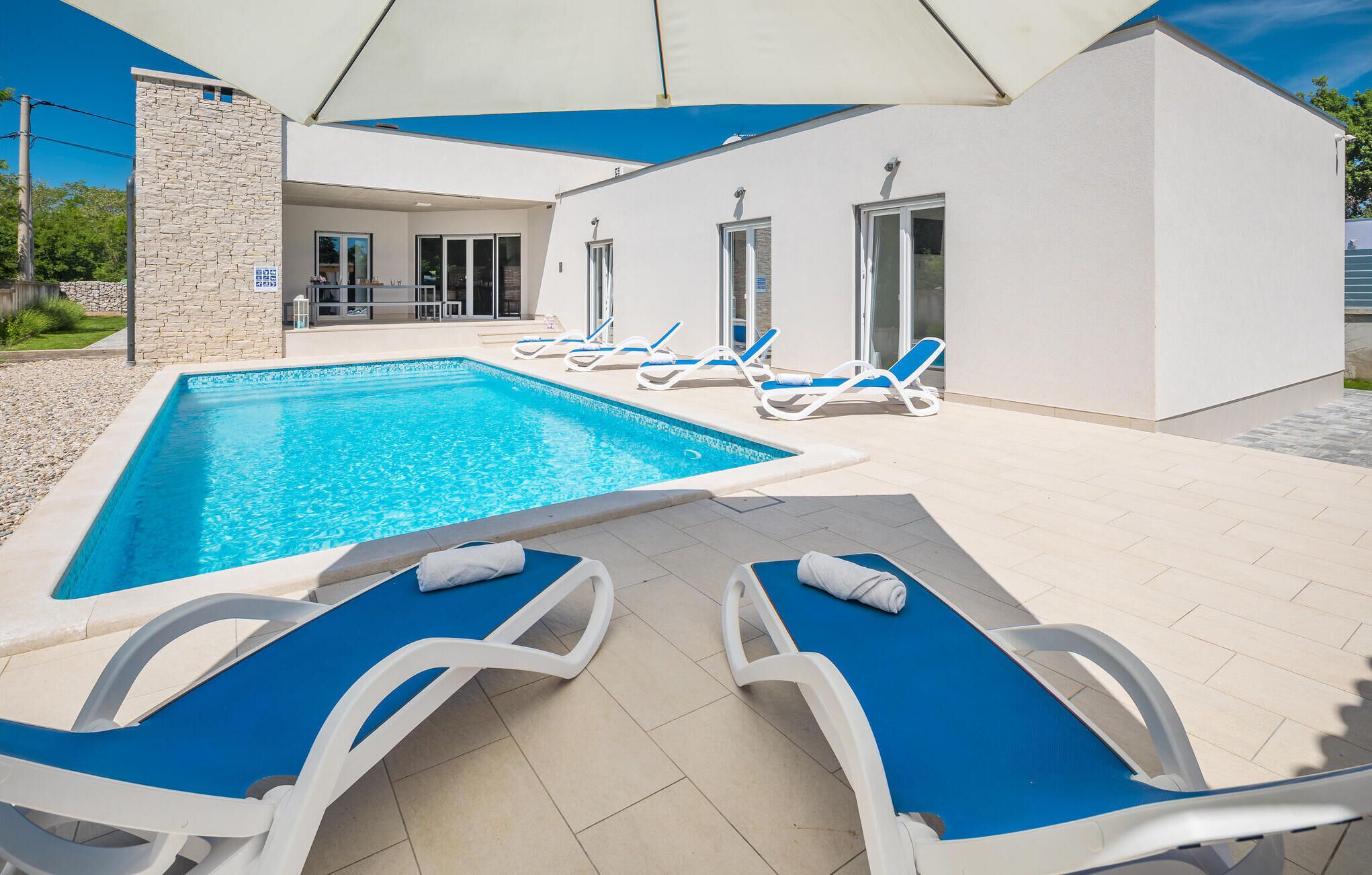 Ein Poolbereich mit rechteckigem Pool, Liegestühlen und einer überdachten Sitzgelegenheit.