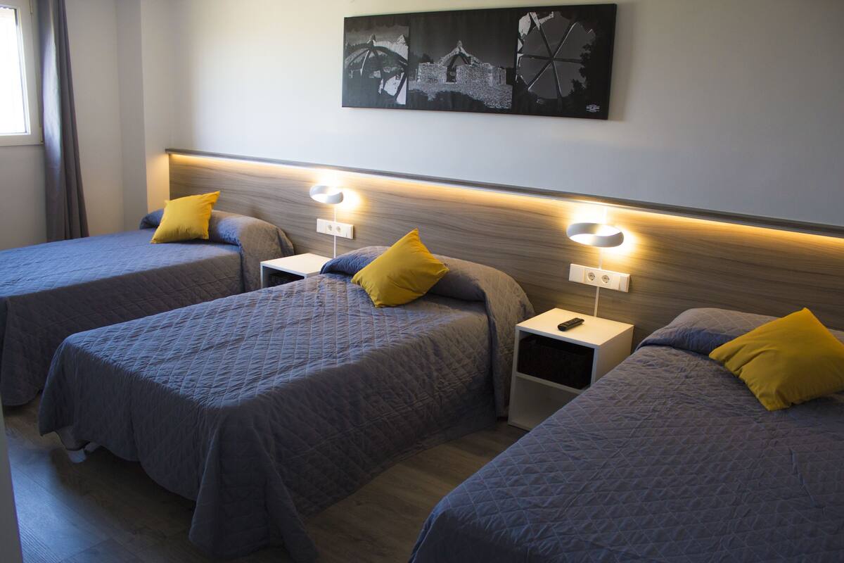 Habitación de hotel con tres camas, cada una con cabecero y mesitas de noche.
