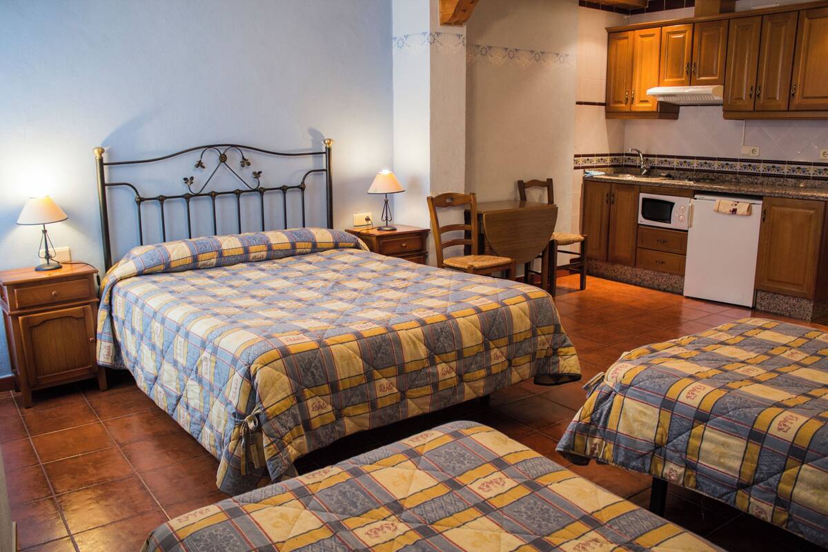 Un dormitorio con dos camas, una mesita de noche, una silla y una kitchenette.