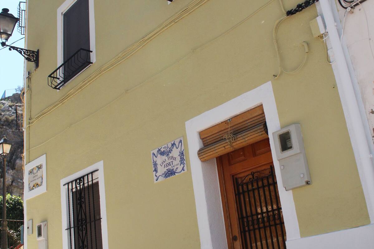Un edificio de dos pisos con fachada amarilla, una puerta de madera y un balconcito.