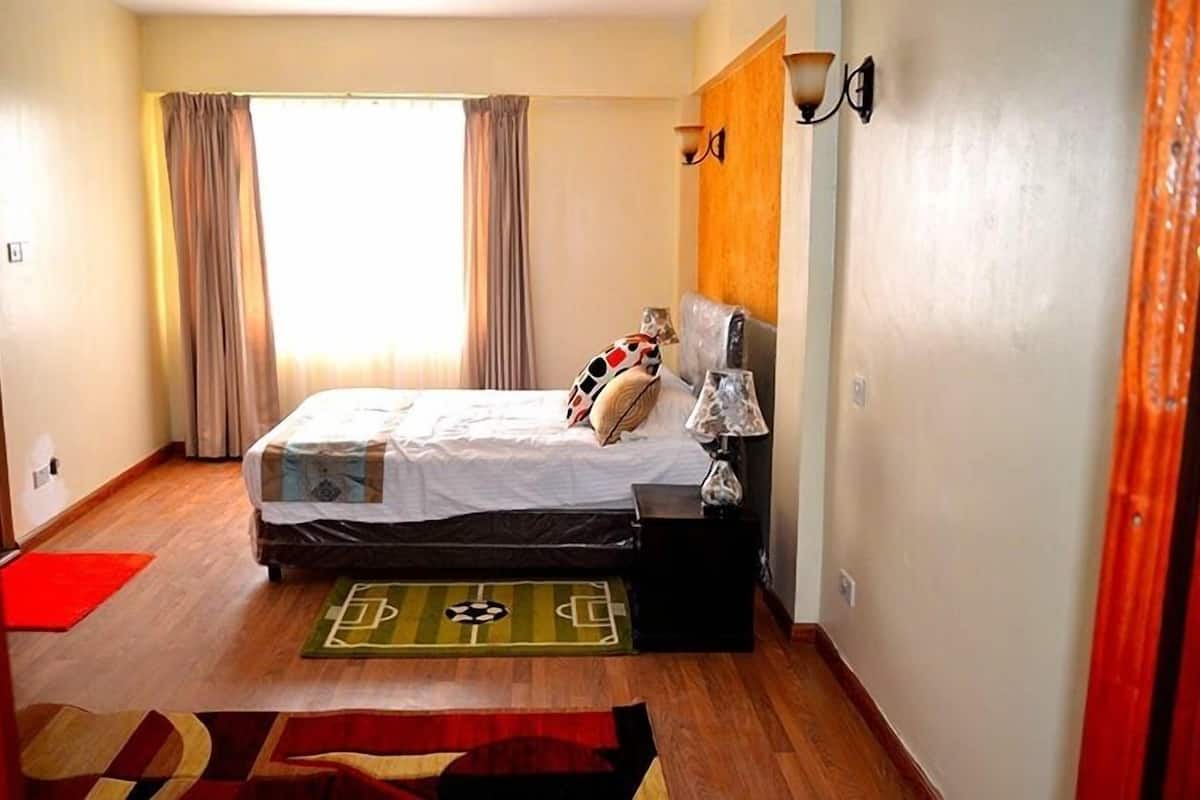 A bedroom with a bed, a nightstand, a lamp, and a window with curtains.