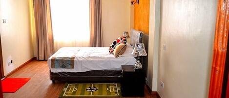 Un dormitorio con cama, mesita de noche, lámpara y ventana con cortinas.