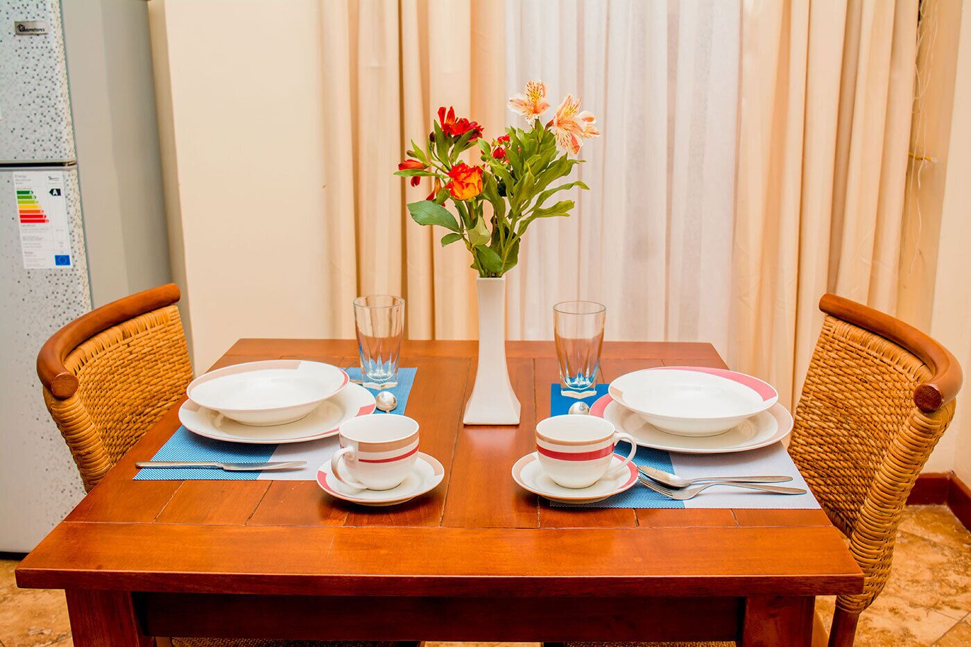 A dining table set with plates, cups, and a vase of flowers.