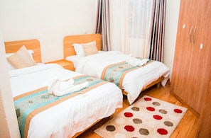 A hotel room with two beds, a wooden wardrobe, and a patterned rug. - Vela Suites (Nairobi)
