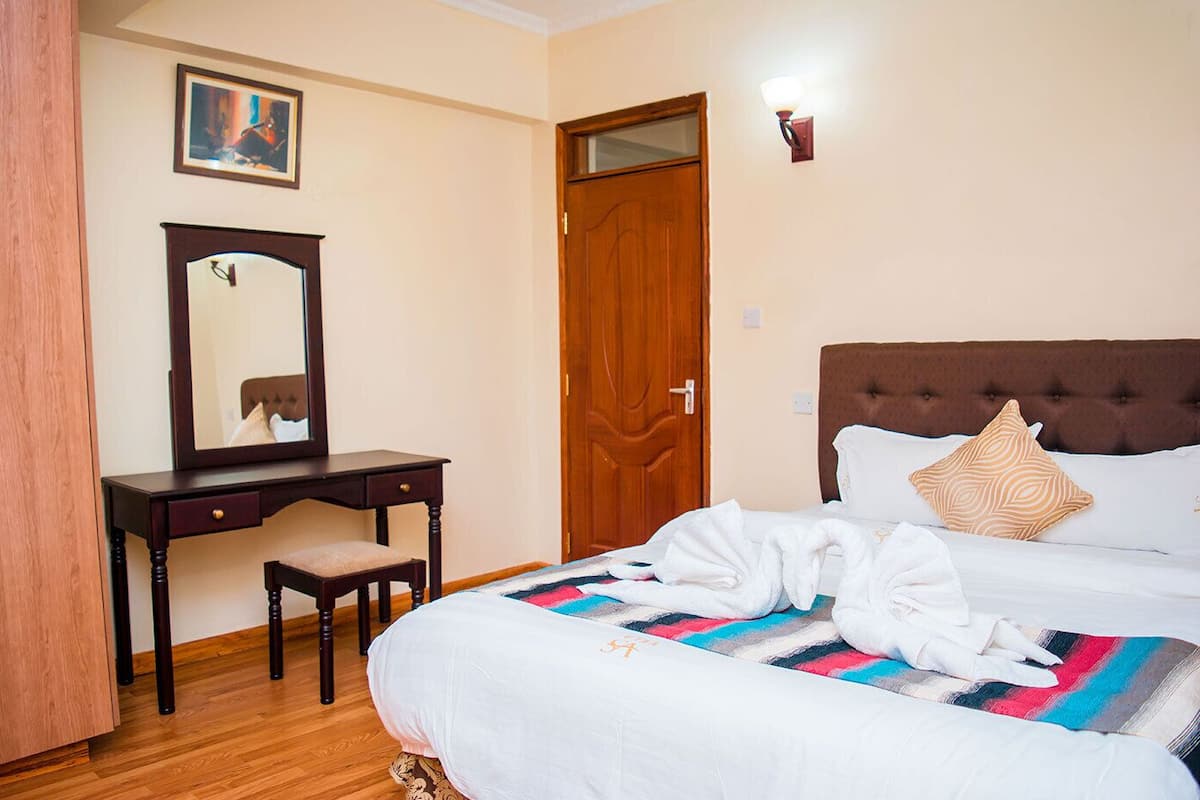 A hotel room with a bed, a wooden desk with a chair, a mirror, and a door.