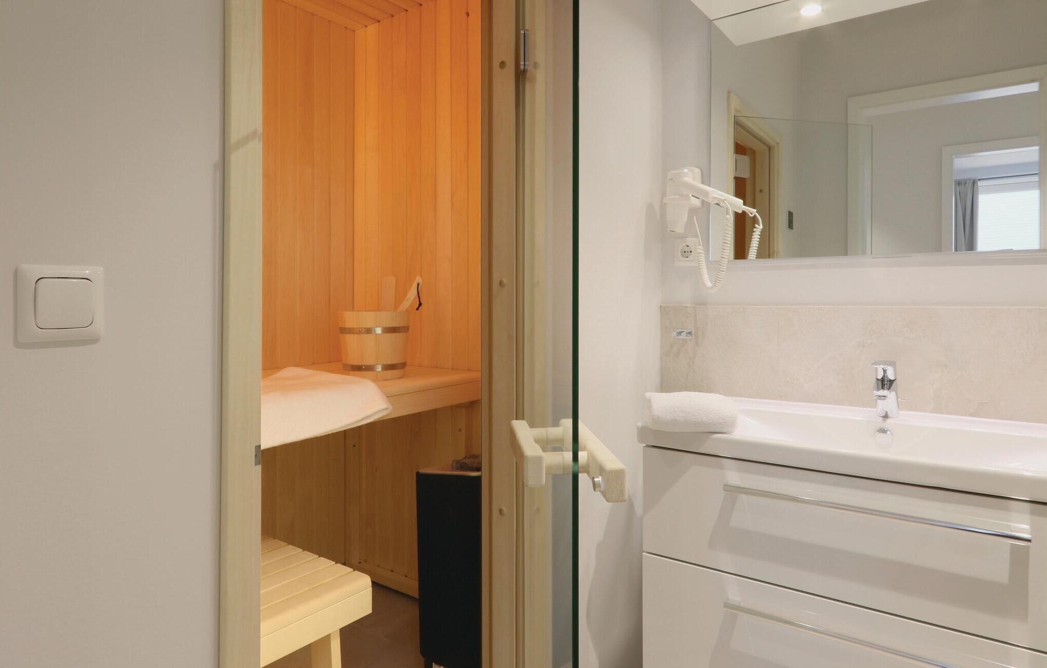 A modern bathroom with a wooden sauna, a white sink, and a large mirror.