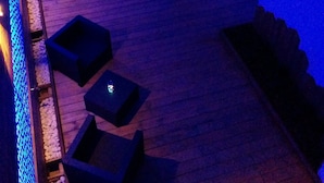 Un área de sala de estar tenuemente iluminada, con piso de madera, varias opciones de asiento como sofás y mesitas, y un revestimiento de pared con diseño.