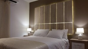 Un dormitorio moderno con una cama grande, dos mesitas de noche con lámparas y un cabecero con líneas iluminadas.