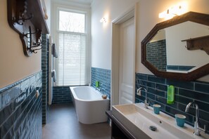 A bathroom with a bathtub, a sink with two cups, a mirror, and a towel rack. - Boutique Hotel De Blauwe Pauw ('s-Hertogenbosch)