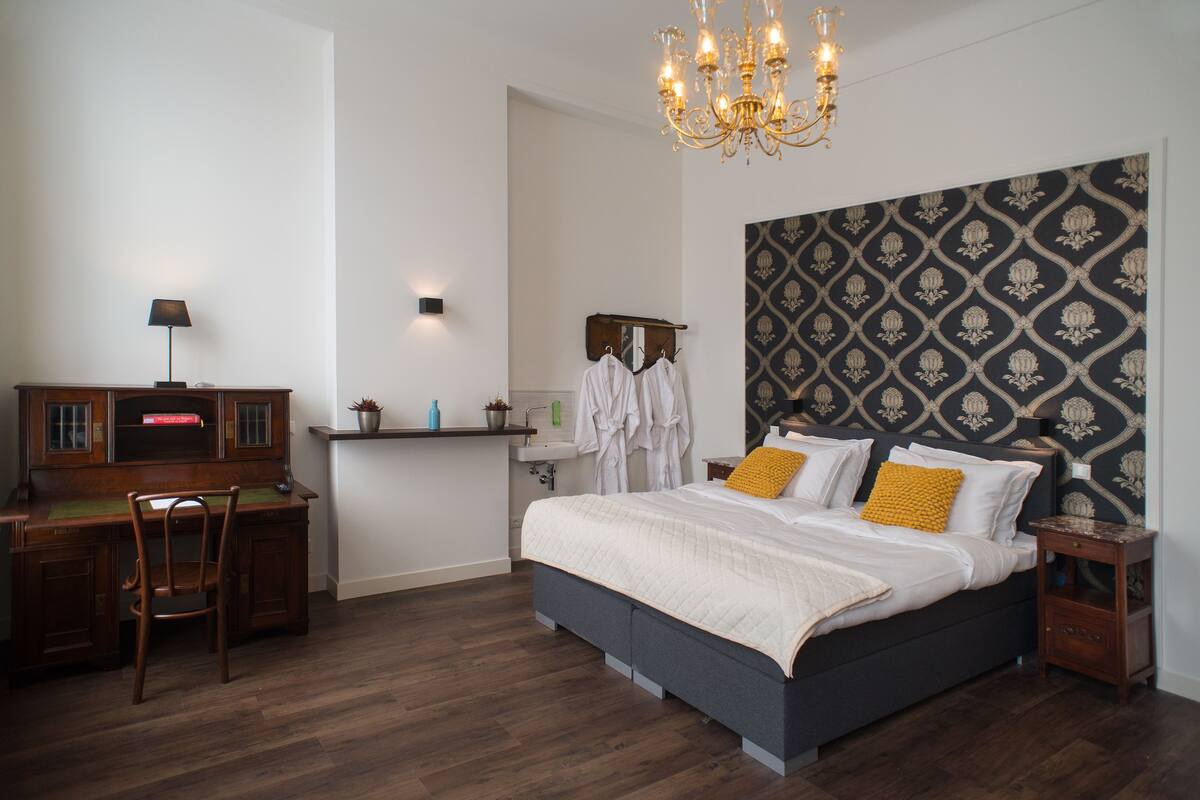 Une chambre à coucher comprenant un lit, un bureau, une chaise, une table de chevet, un lustre et une tête de lit à motifs.