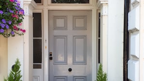 A white door with a decorative archway, flanked by two potted plants and a hanging flower basket. - Canterbury Lodge (Canterbury)