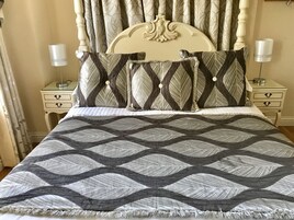 Una cama con colcha estampada, dos mesitas de noche con lámparas y un cabecero con cortinas.