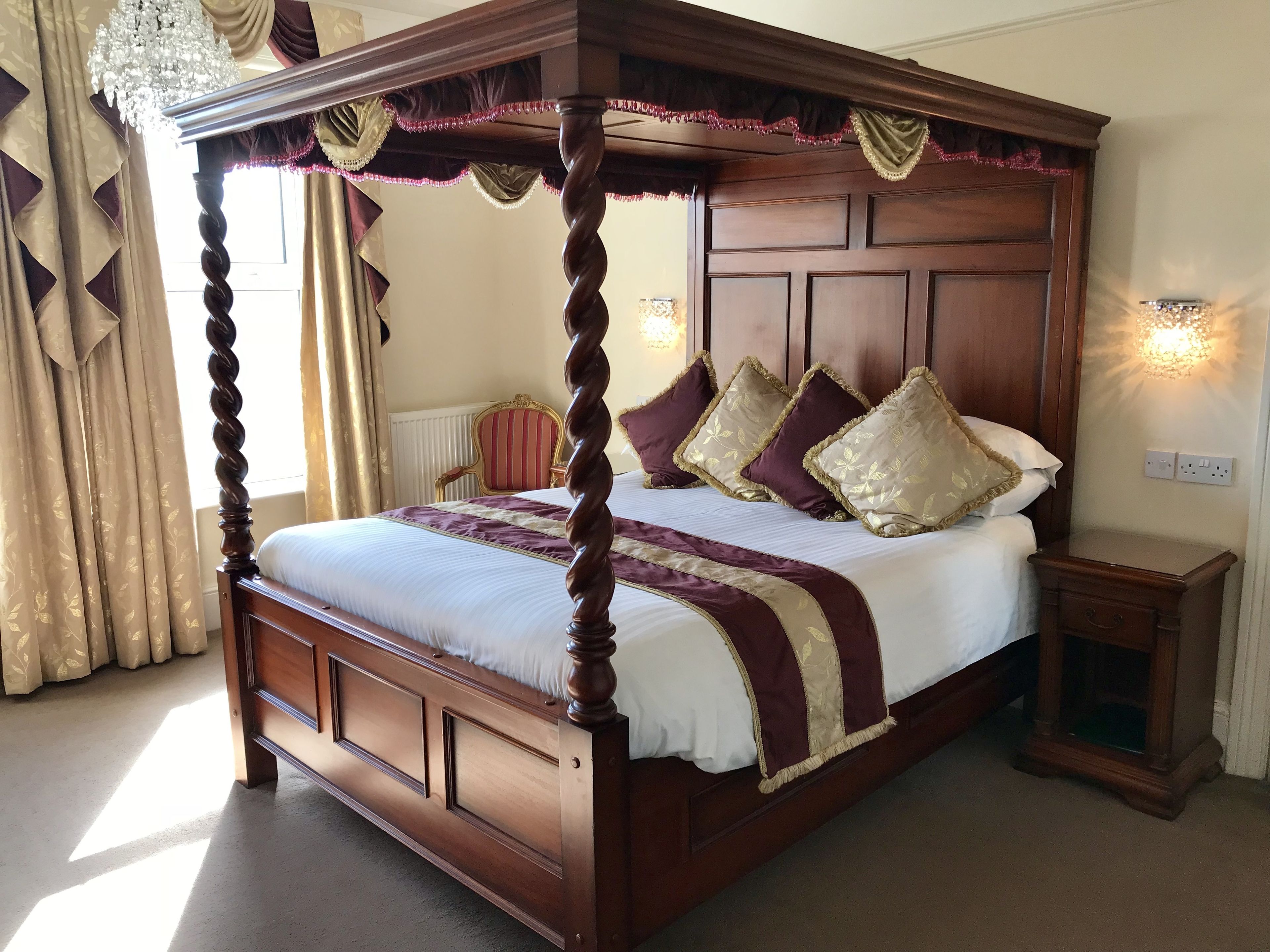 A four-poster bed with a wooden frame, a white and maroon bedspread, and matching pillows.