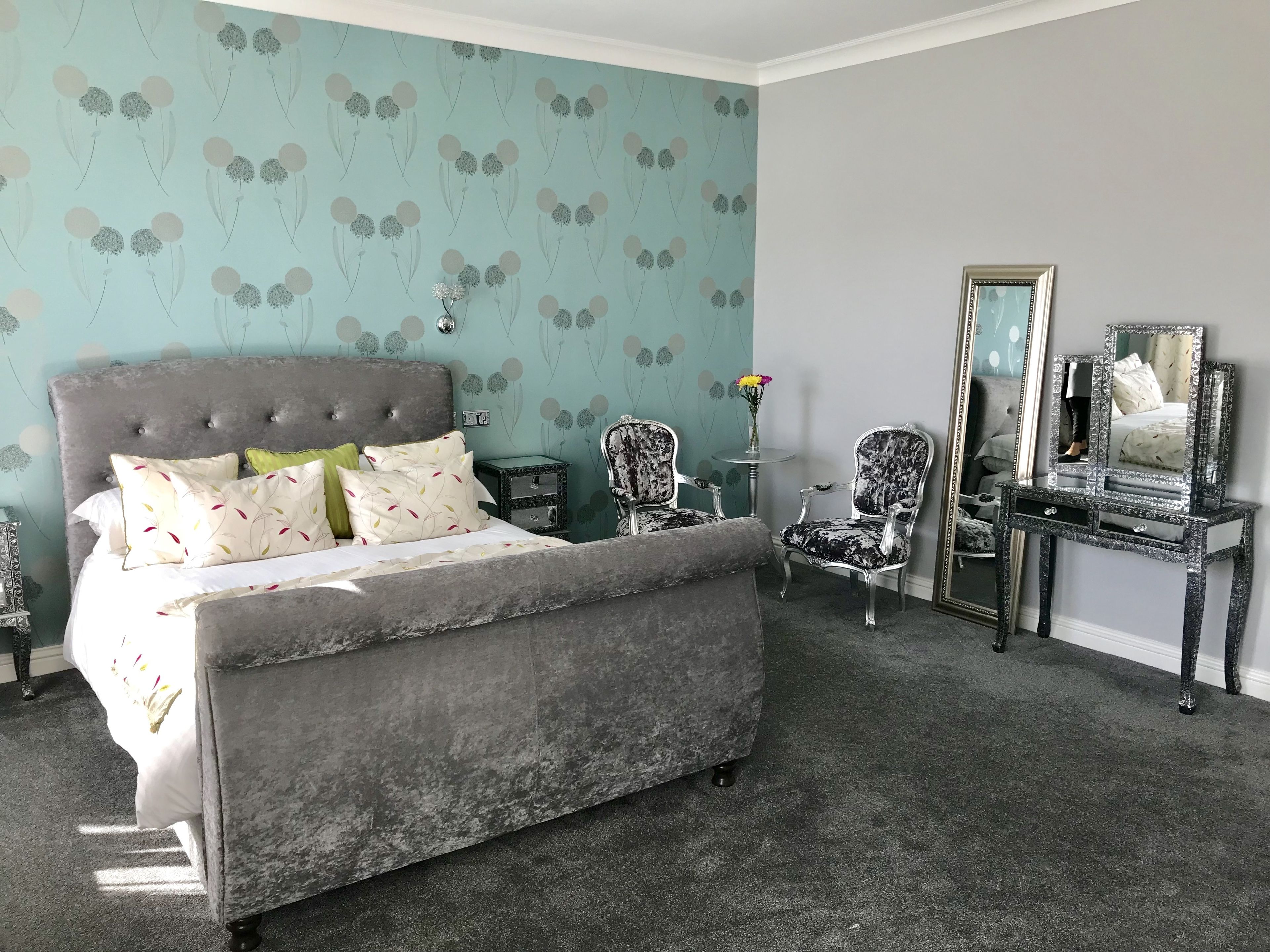 A bedroom with a grey upholstered bed, a vanity with a mirror, and a chair.