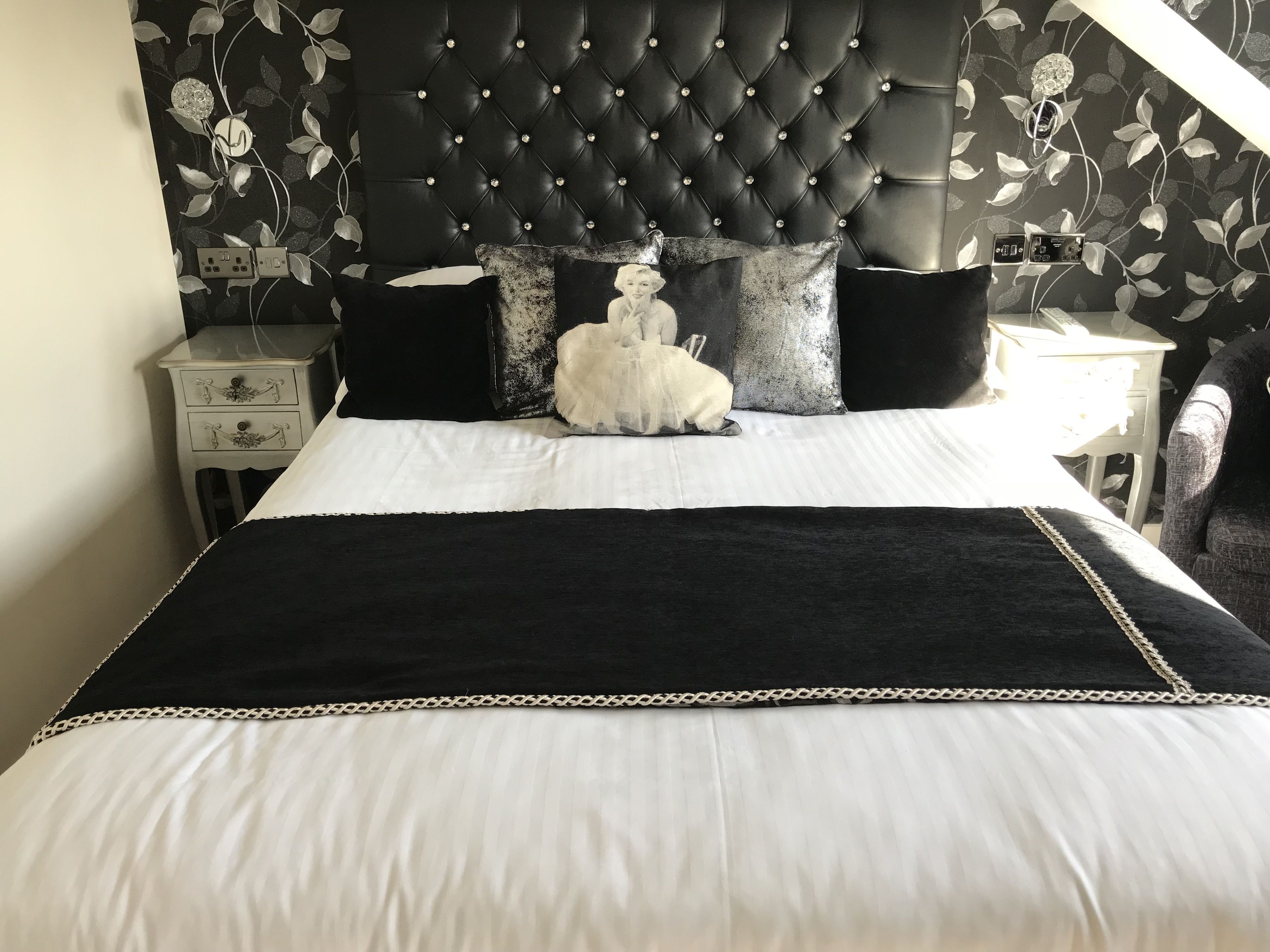Ein Bett mit schwarzem Kopfteil, weißer Bettwäsche und Zierkissen.