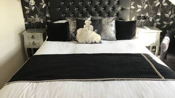 Una cama con cabecera negra, ropa de cama blanca y almohadas decorativas.