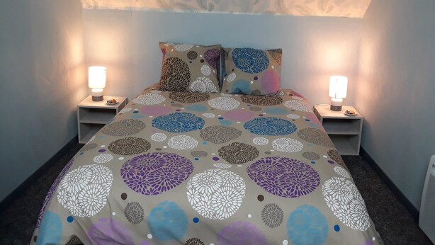 Ein Schlafzimmer mit einem gemusterten Bettbezug, zwei Nachttischlampen und einer dekorativen Decke.