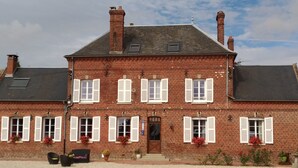 Ein zweistöckiges Backsteinhaus mit weißen Fensterläden, einem mittleren Eingang und einem Schotterweg.