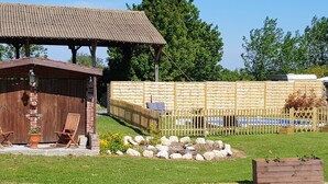 Ein rustikaler Außenbereich mit Holzzaun, einem kleinen Garten mit Steinen und Blumen sowie einer Holzhütte mit Stühlen.