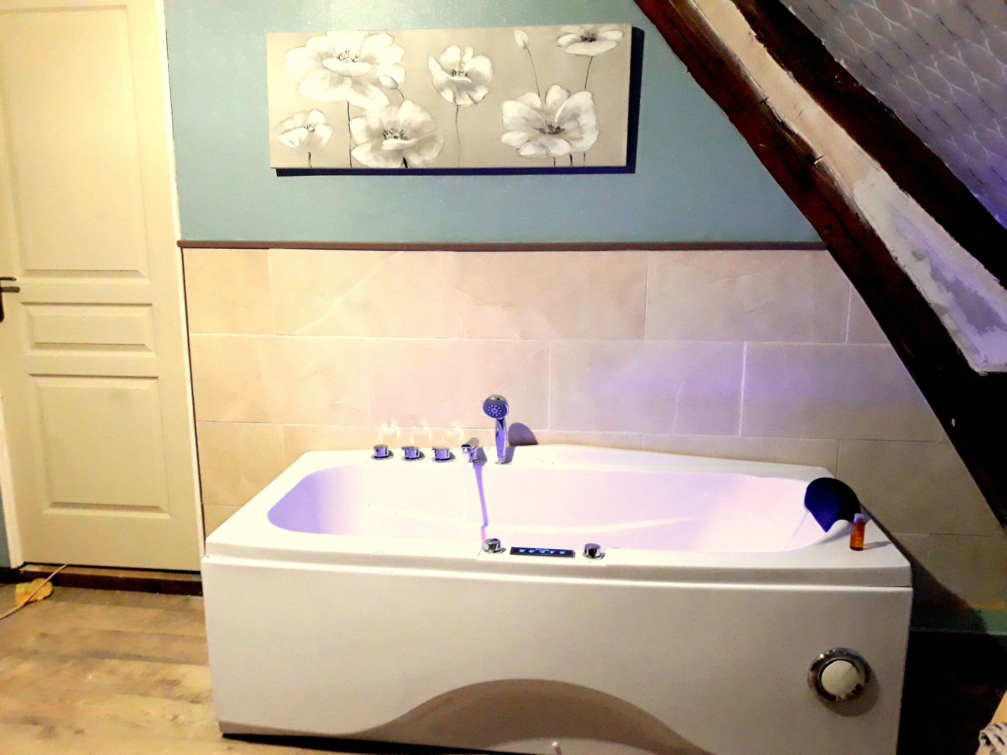 Ein Badezimmer mit einer weißen Badewanne, einem Wandbild mit weißen Blumen und einer gefliesten Wand.