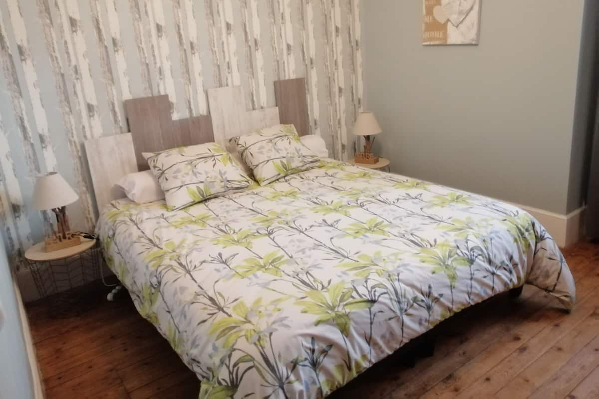 A bedroom with a floral bedspread, two bedside tables with lamps, a wooden headboard, and a wall-mounted picture.
