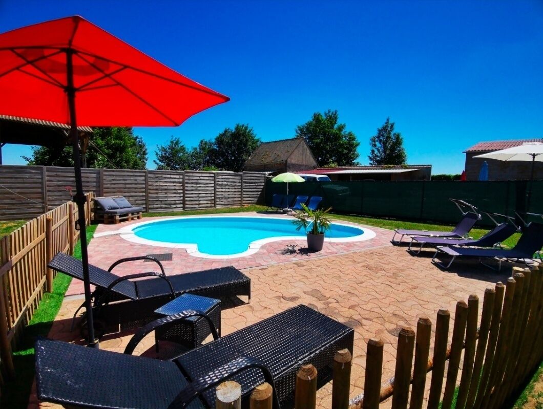 Un jardin avec une piscine, des chaises longues et un parasol rouge.