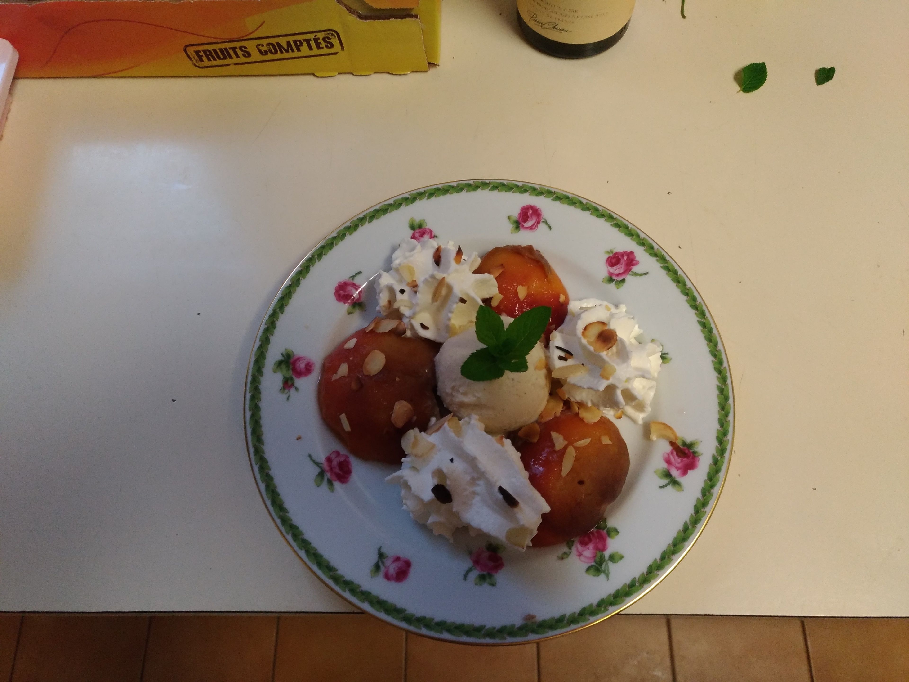 Un plato de postre con compota de frutas, nueces y crema batida sobre un plato estampado con motivos florales.