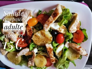 Une salade composée de poulet grillé, de tomates, d’olives et de fromage, servie dans une assiette blanche.