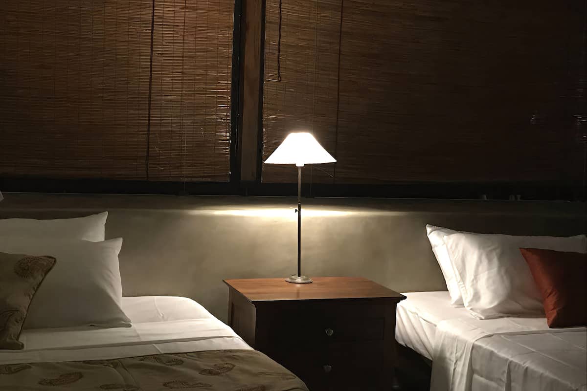 Quarto de hotel com duas camas, uma mesa de cabeceira e uma luminária.