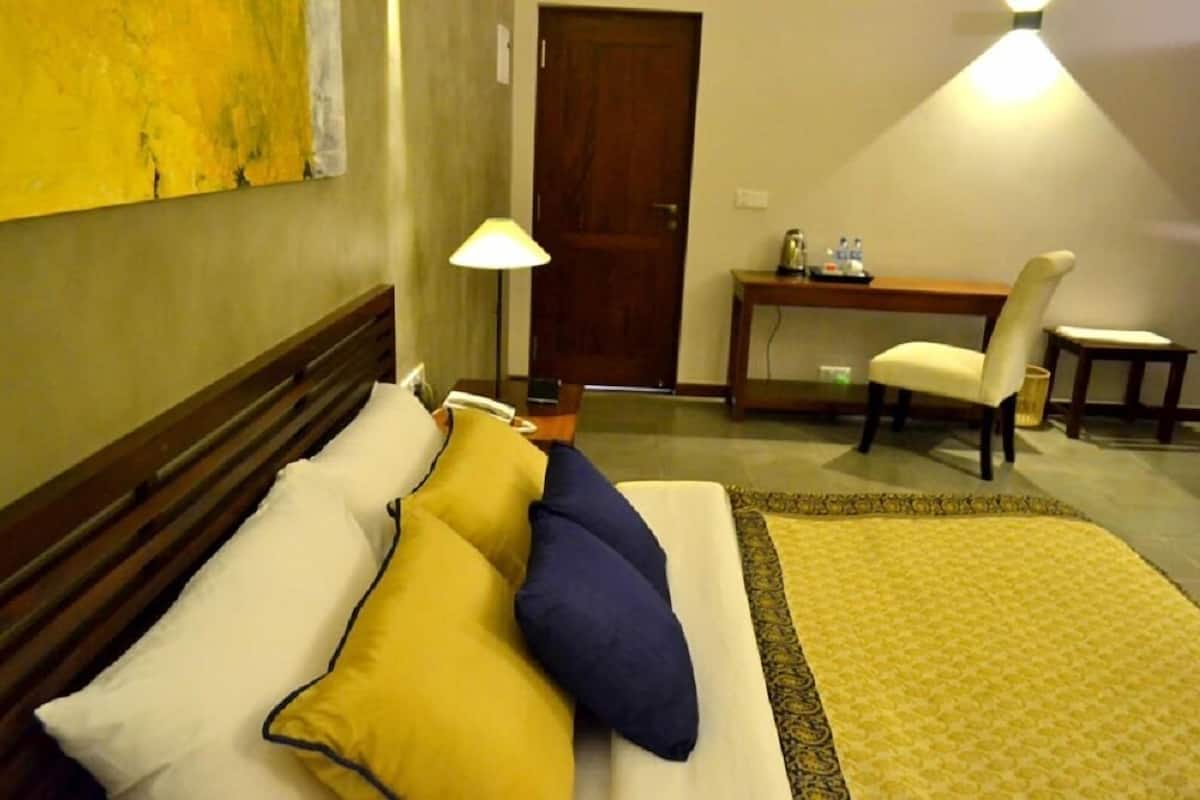 Quarto de hotel com cama, escrivaninha, cadeira e abajur.