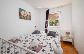 Quarto com cama, mesa de cabeceira, luminária, janela com cortinas e um quadro na parede.