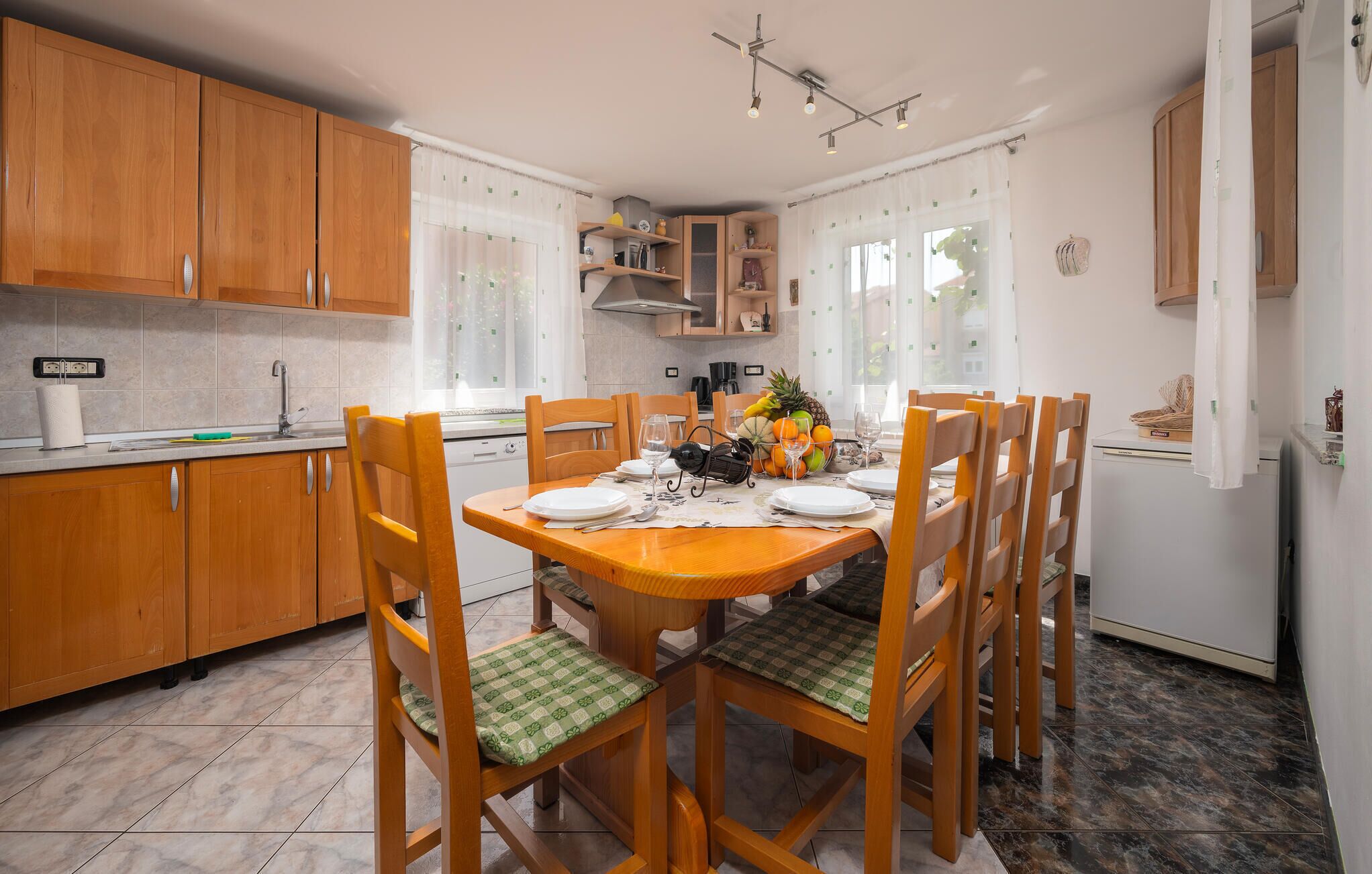 Een kleine keuken met houten kastjes, een eettafel gedekt voor vier personen en een fruitschaal op de tafel.