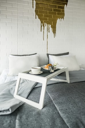 A neatly made bed with a white frame, a tray with a cup and croissant, and a white brick wall with a dripping effect. - Design hotel Rooms & Rumors (Odesa)