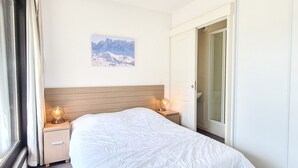 Une chambre d’hôtel avec un grand lit, une tête de lit en bois, deux tables de chevet avec des lampes, un tableau au mur et une porte coulissante donnant sur la salle de bain.