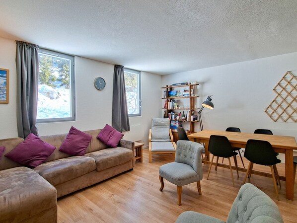 A cozy living room with a sofa, chairs, a dining table, and a bookshelf.