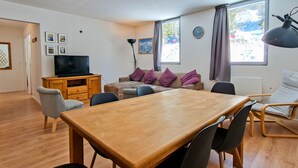Ein Wohnzimmer mit Holztisch, Stühlen, einer Couch, einem Fernseher und einer Lampe.