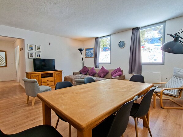 A living room with a wooden table, chairs, a sofa, a TV, and a lamp.