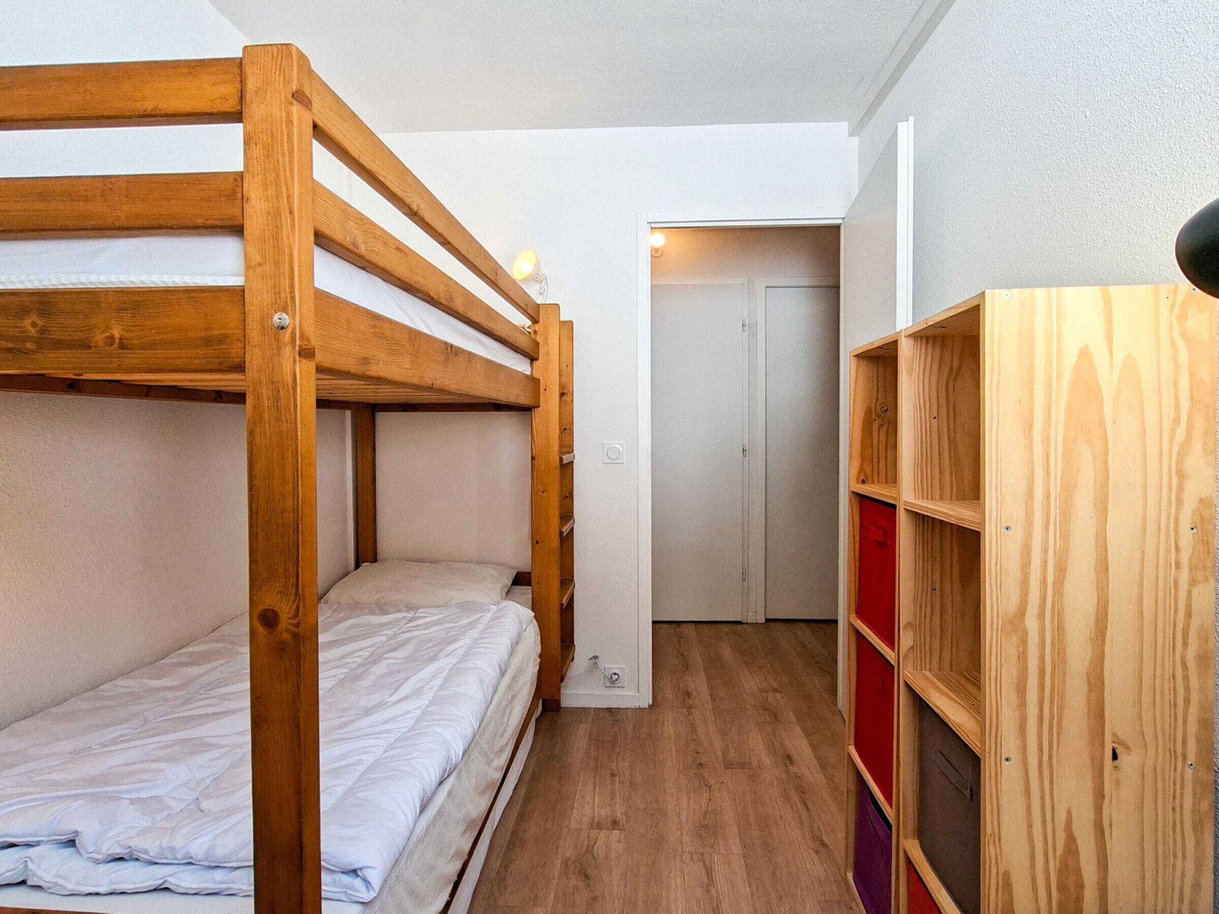 A bunk bed room with a wooden headboard, a small wooden cabinet, and a door in the background.