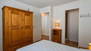 Ein Schlafzimmer mit großem Holzschrank, Nachttisch mit Lampe und weißer Bettdecke.