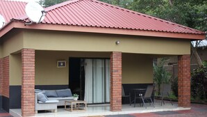 A covered outdoor seating area with a sofa, chairs, and a small table. - Sweet Holiday Homes (Victoria Falls)