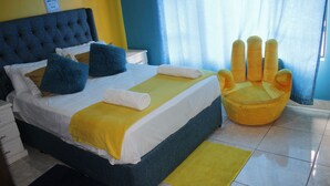 A bed with a blue headboard, white bedding, and blue and yellow pillows. There is a yellow armchair and a yellow rug on the floor. - Sweet Holiday Homes (Victoria Falls)