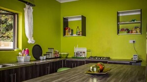 A kitchen with a wooden countertop, a sink, and a window with a curtain. There are shelves with food items and a kettle on the counter. - Sweet Holiday Homes (Victoria Falls)
